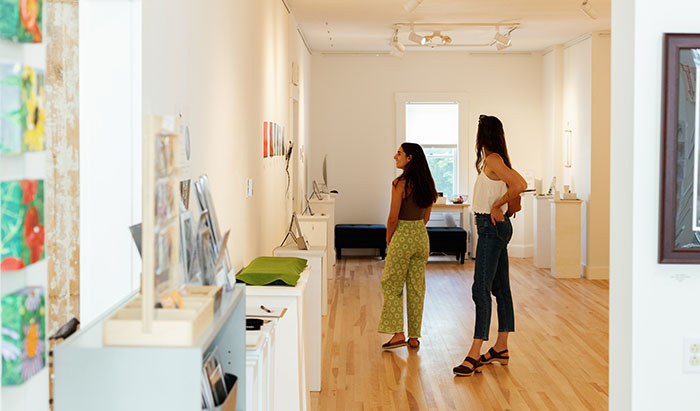 2 women looking at art on the wall inside an art gallery.