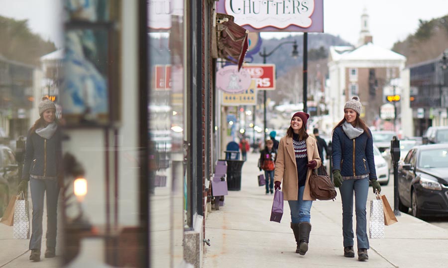 two woman walking down a main street with shopping bags in winter