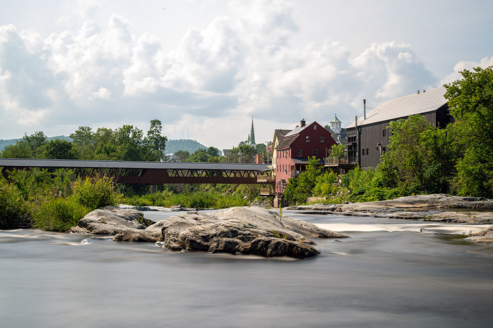 a long covered bridge over a river connecting to a red building