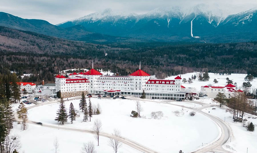 aerial view of a large white hotel with a red roof surrounded by snow
