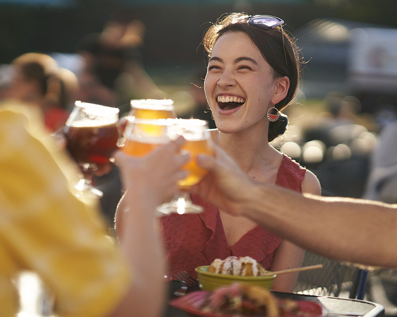 people clinking beer classes together outdoors at a table