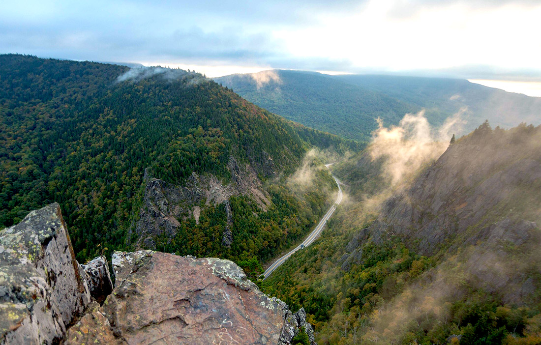a view off a rocky cliff of  a road cutting through large mountains