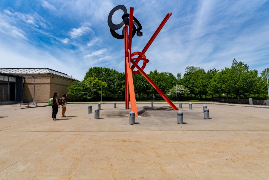Visitors looking at a red metal sculpture outside a museum building