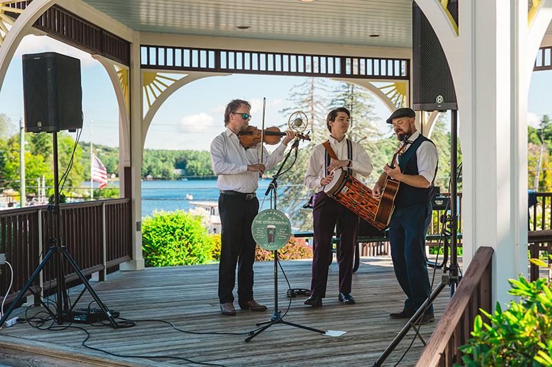 3 musicians playing on a gazebo next to the water