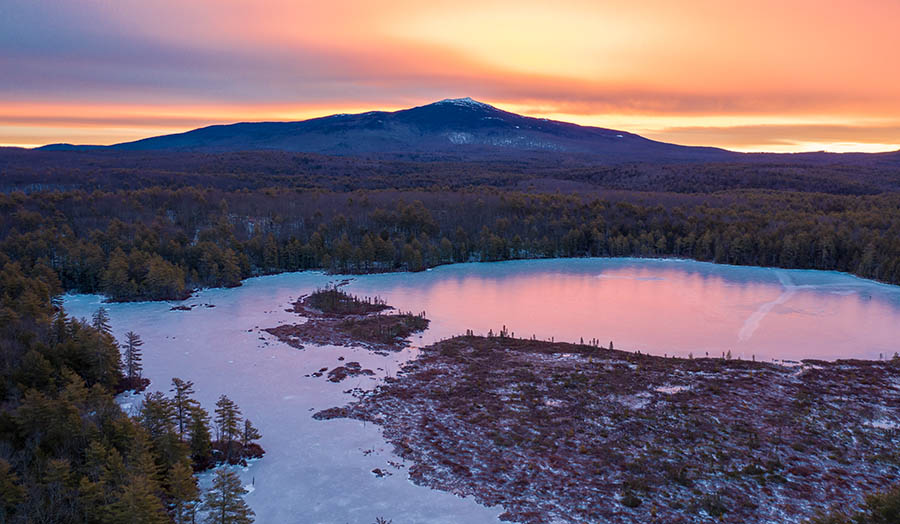 a view of a mountain peak and frozen icy  lake at sunset