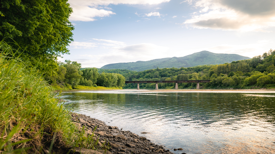 a view of a covered bridge over a river with mountain in background
