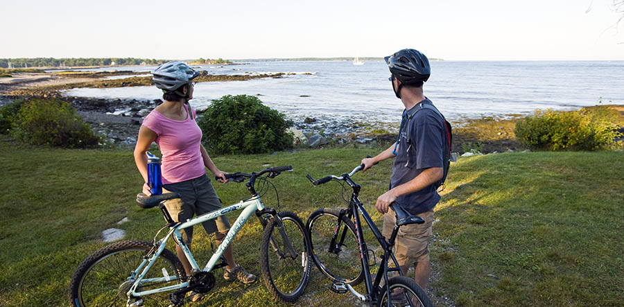 a man and woman standing with bikes admiring an ocean view