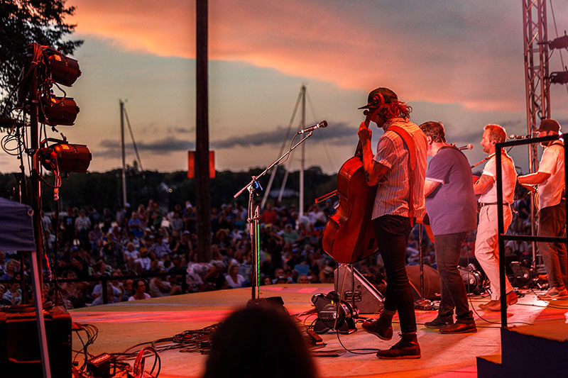 a band playing on stage at sunset, facing the crowd