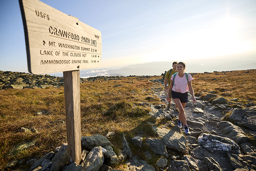 two hikers on a rocky trail near a trail sign